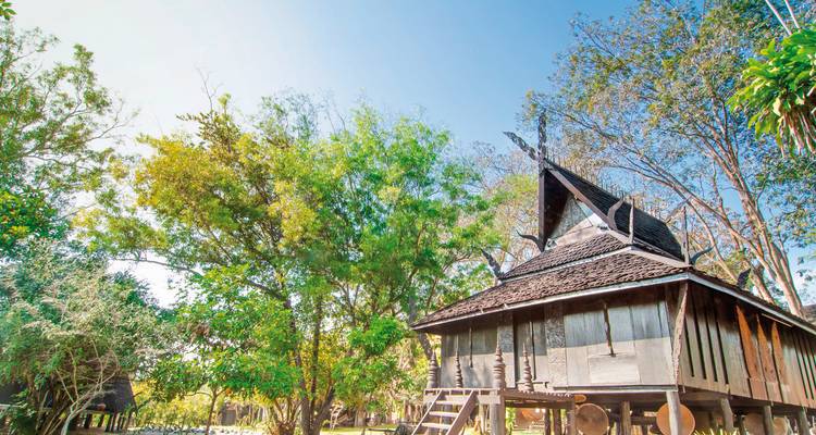 Traditional wooden house in a garden setting under a blue sky.