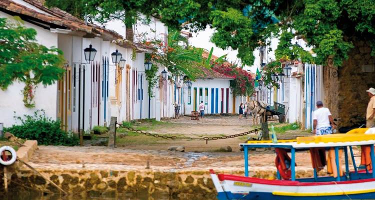 Rue coloniale colorée avec une charrette à cheval et des piétons.