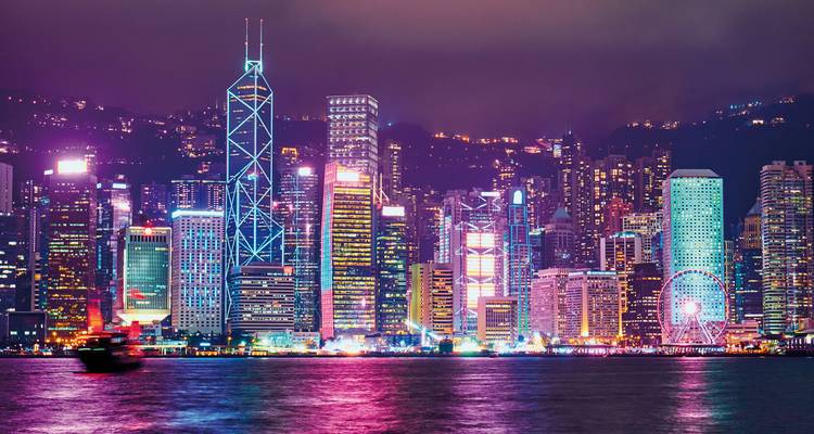 Vue nocturne de l'horizon de Hong Kong avec des bâtiments illuminés et leur reflet dans le port.