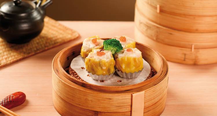 Dim Sum in einem Bambusdämpfer auf einem Holztisch, Hong Kong Küche.