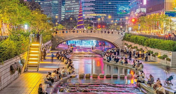 Lebendiges Stadtgebiet mit einem Bach, beleuchteten Brücken und Menschen, die eine Nachtszene genießen, Seoul, Südkorea.
