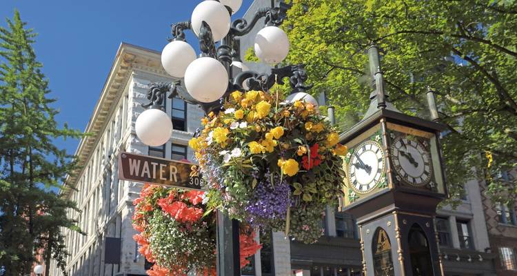 Historic clock and ornate street lamp amidst flowers in a city setting.