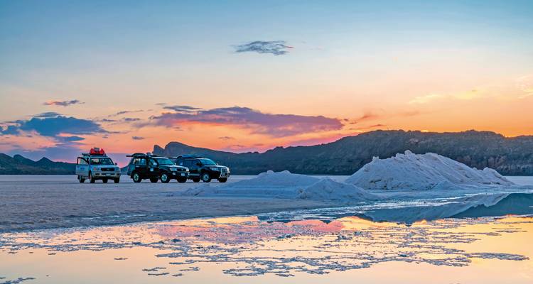 4x4-Fahrzeuge auf einer weiten Salzebene bei Sonnenuntergang mit Hügeln in der Ferne.