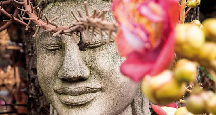 Steinstatue mit blumigem Vordergrund.