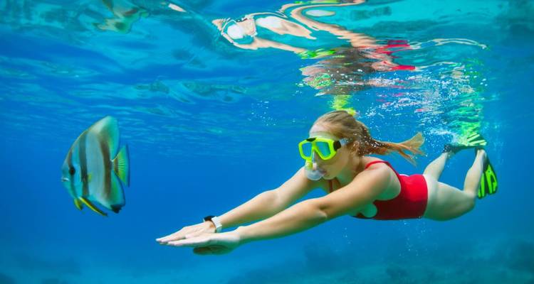 A person snorkeling underwater with a fish nearby.