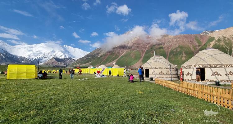 Yourtes et tentes jaunes sur un champ d'herbe avec des montagnes en arrière-plan.