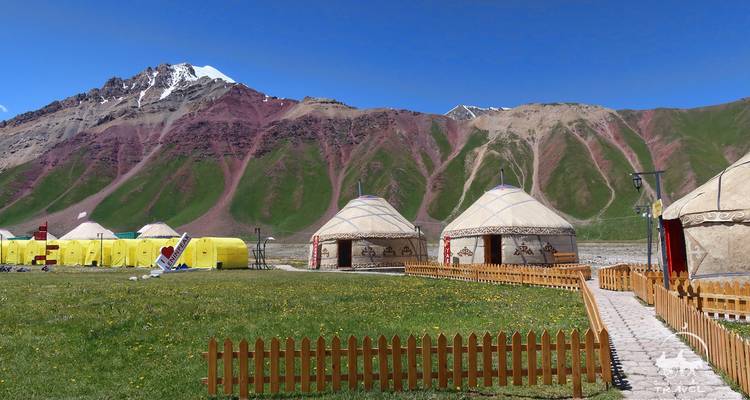 Yourtes et tentes sur une herbe luxuriante avec des montagnes colorées en arrière-plan.