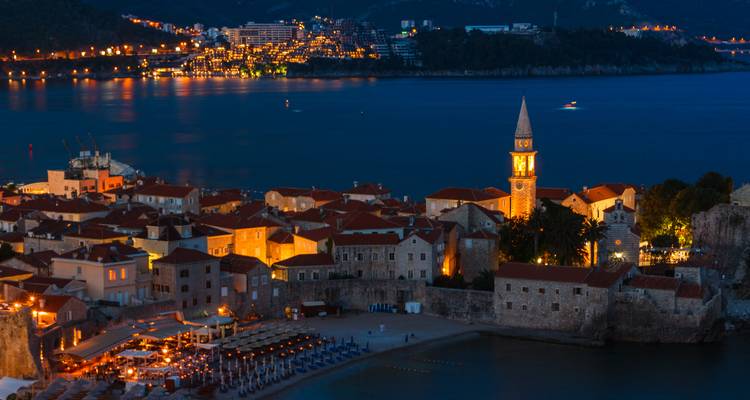 Vue nocturne d'une ville côtière avec des bâtiments illuminés.