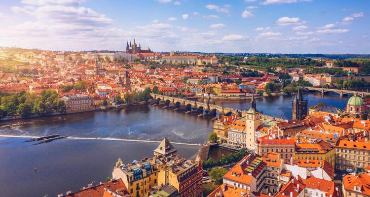 Aerial panorama of Prague with Vltava River bridges and Prague Castle illuminated by warm afternoon light.