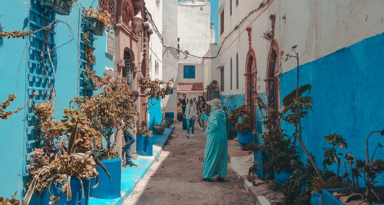 Narrow alley painted blue and white with locals and potted plants in Rabat’s medina.