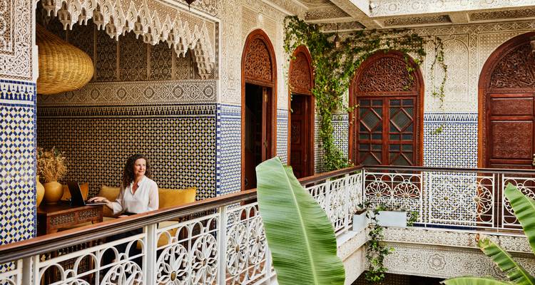 Elegant riad interior with patterned tiles where a woman relaxes at a wooden desk.