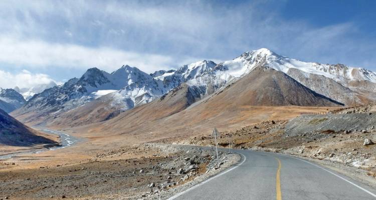 Scenic view of a winding road through a mountain range with snow-covered peaks.