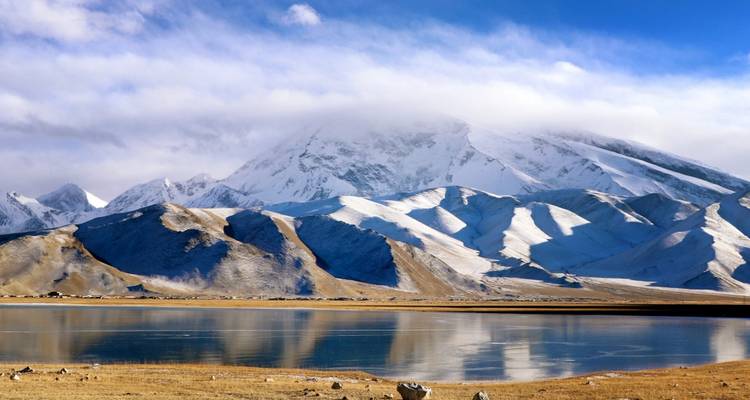 Snow-covered mountains and a serene lake under clouded skies.