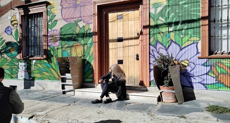 Escena callejera con una persona sentada frente a un mural.