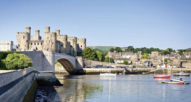 Château de Conwy au bord d'une rivière avec des bateaux amarrés.