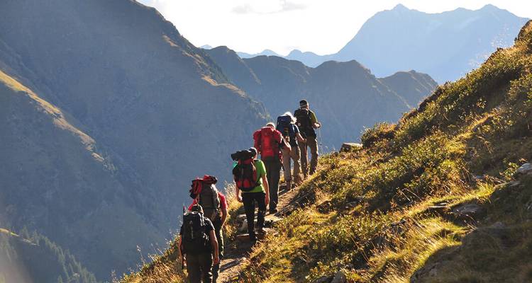 Wanderer, die einen steilen Bergpfad unter klarem Himmel überqueren.