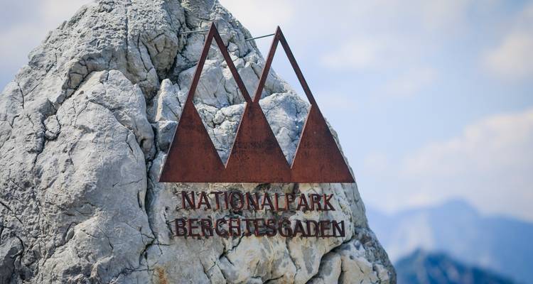 Ein Holzschild für den Nationalpark Berchtesgaden vor einem felsigen Hintergrund.