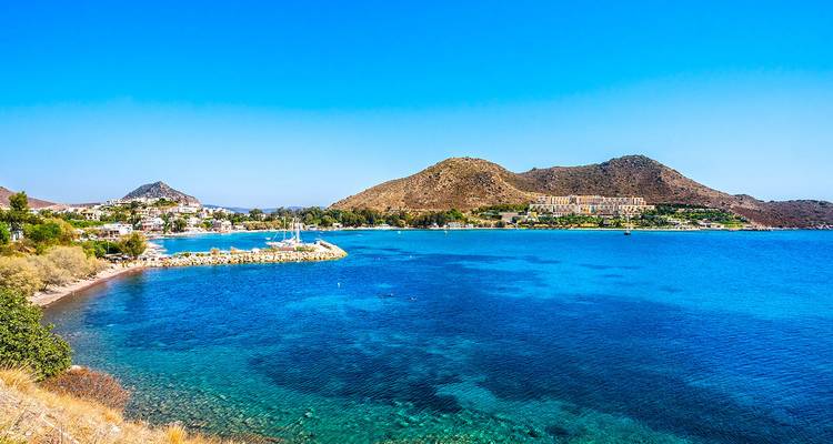 Bahía turquesa vibrante enmarcada por colinas áridas y cielo azul cristalino en la costa del Egeo