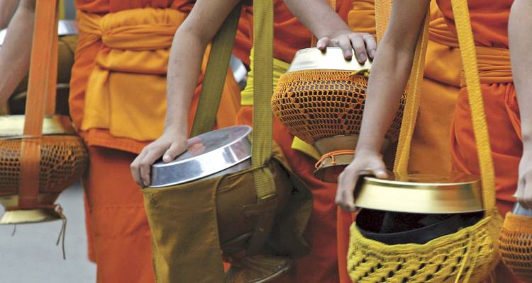Close-up of monks in orange robes holding alms bowls with shoulder straps