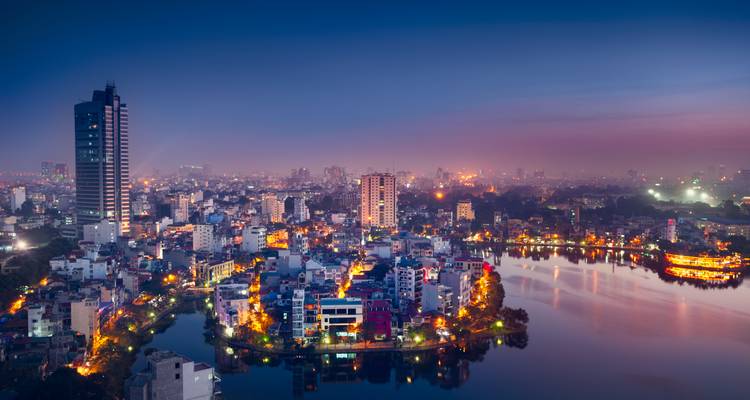Night skyline of Hanoi glowing with city lights around a reflective lake.