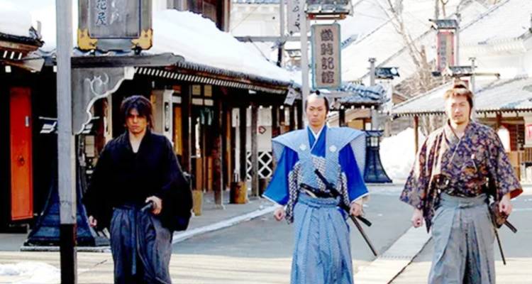 Men dressed in traditional samurai outfits walking down a snowy street.