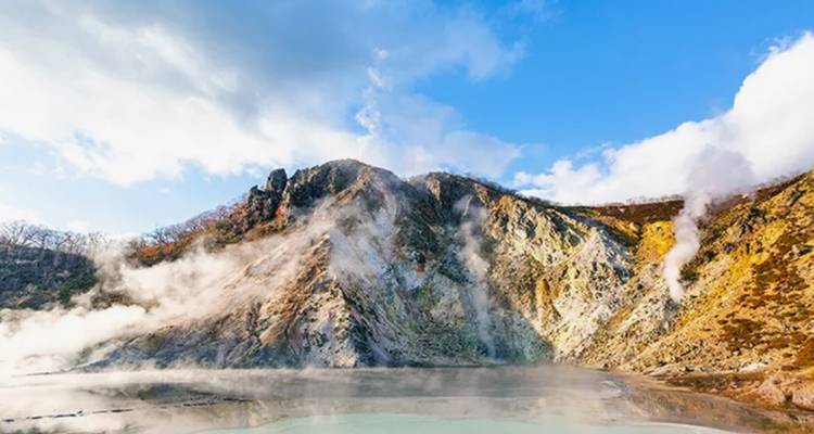 Colorful volcanic landscape with steam rising under a clear blue sky.