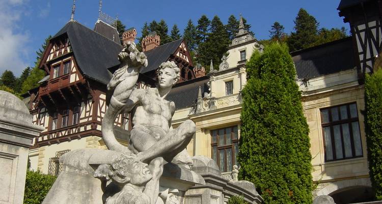 Statue devant un grand bâtiment historique avec un environnement luxuriant.