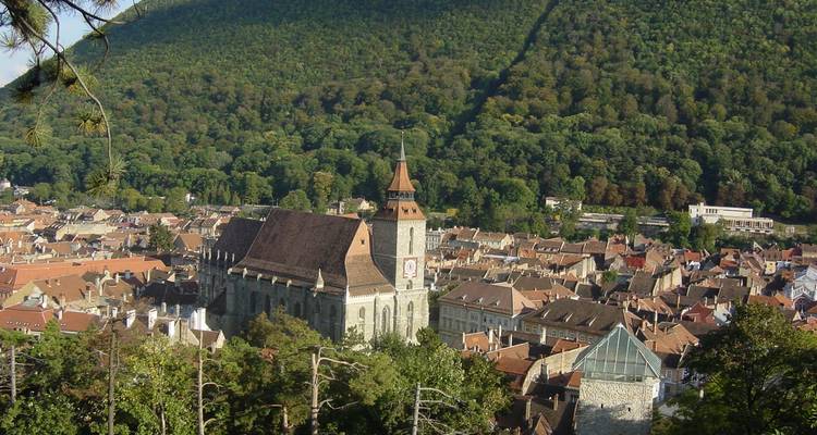 Vue aérienne d'une grande église dans une ville entourée d'arbres et de collines.