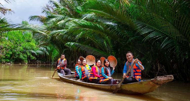 A group of people in a wooden boat navigating a river surrounded by dense palm trees.