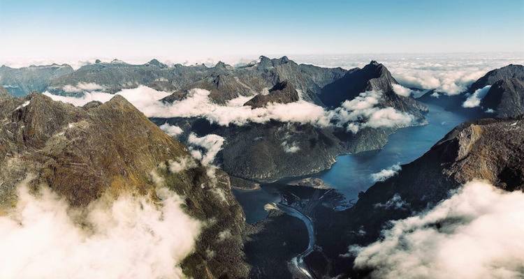 Aerial view of dramatic mountain ranges and fjords under clear skies.
