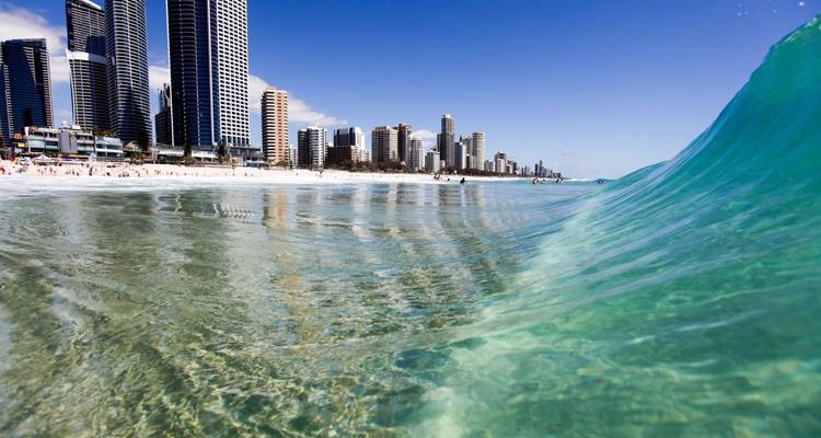 Crystal clear turquoise wave curls in foreground with Gold Coast skyline and beach in distance.