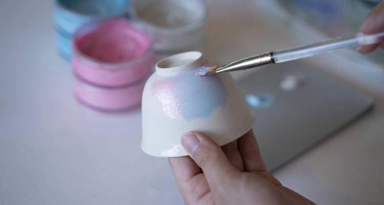 Gros plan d'une main peignant un bol en céramique avec des couleurs pastel.