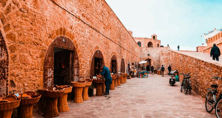 Stone alley with arched shop fronts displaying woven baskets and local crafts.