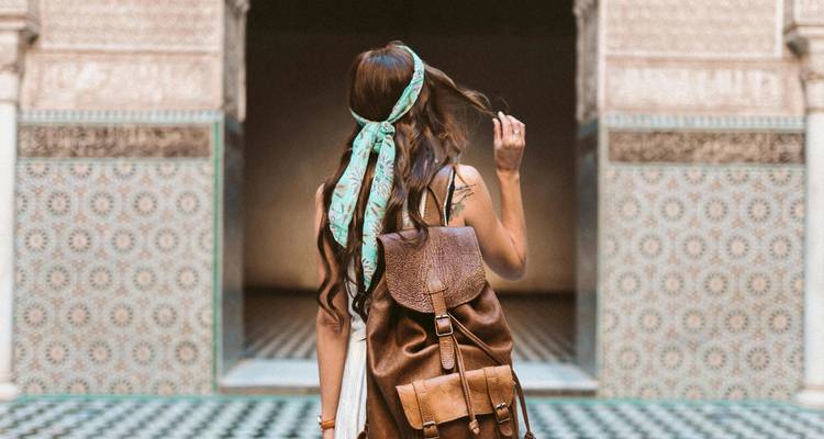Female traveller with retro backpack admiring intricate mosaic tiles in a Moroccan courtyard.