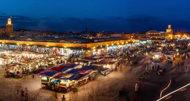 Long-exposure night scene of Jemaa el-Fnaa market with colorful stalls and blurred motion of crowds.