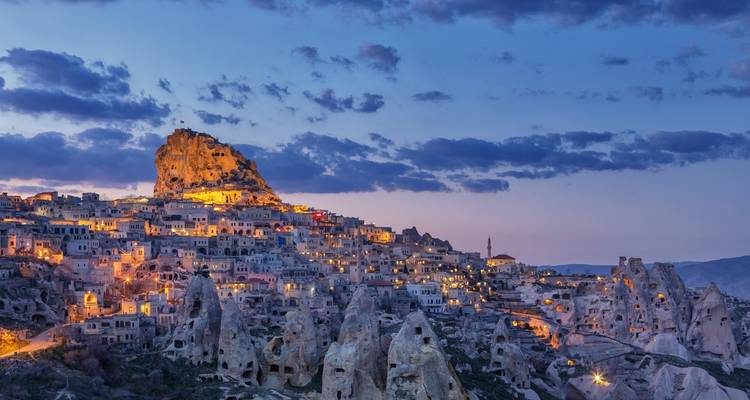 Edificios tallados en roca de Capadocia al atardecer con luces.