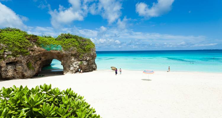 Wit zandstrand met turquoise water, rotsformaties en mensen die van de zon genieten.
