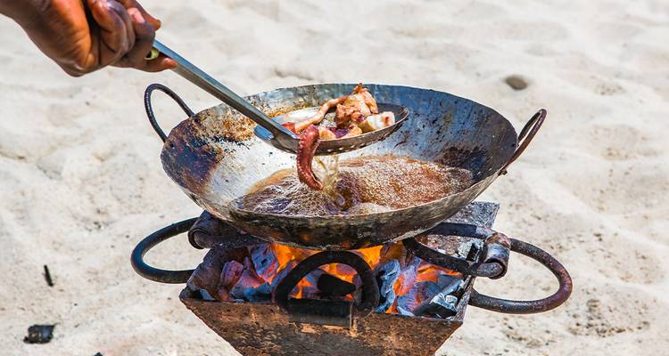 Una persona friendo comida en una sartén grande sobre un fuego al aire libre.