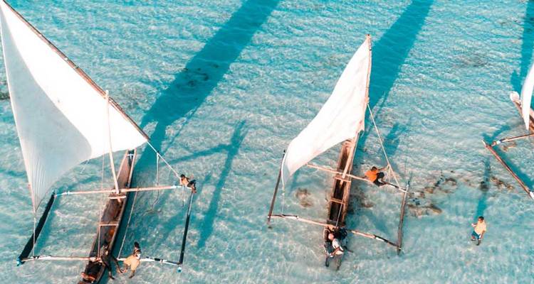 Veleros de madera con velas blancas sobre agua turquesa cristalina creando una escena serena.