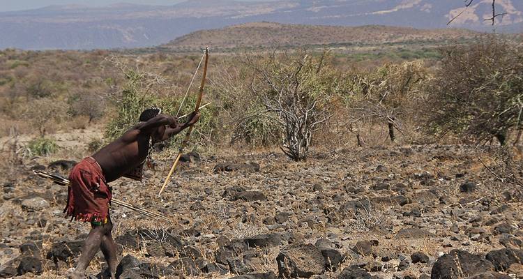 Man with a bow practicing archery in a rocky field.