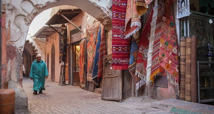 Un homme en vêtements traditionnels marchant dans un magasin de tapis marocains.