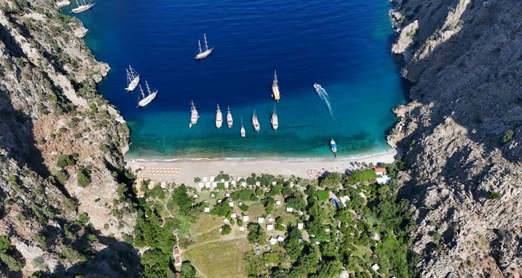 Luftaufnahme eines Küstentals mit Yachten und üppigem Grün.