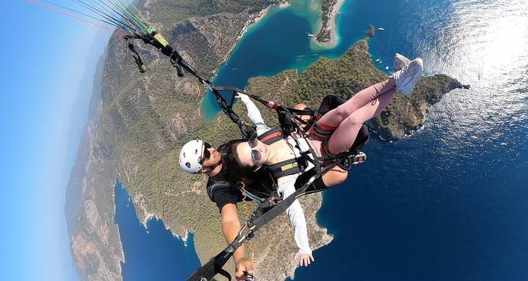 Paraglider, die über eine malerische Küstenlandschaft mit blauem Wasser fliegen.
