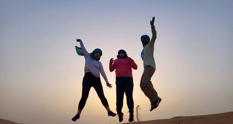 Three people jumping in the desert with the sun setting behind them.
