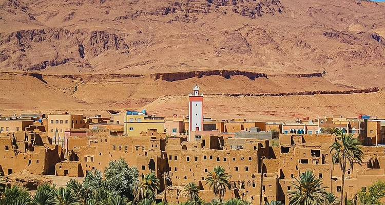 Rustic fortified village at the base of rocky desert mountains.