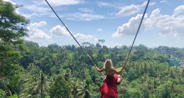 Woman on a swing in a lush green forest.