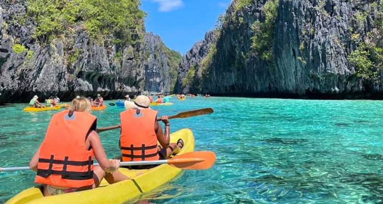 People kayaking on clear turquoise water surrounded by cliffs.