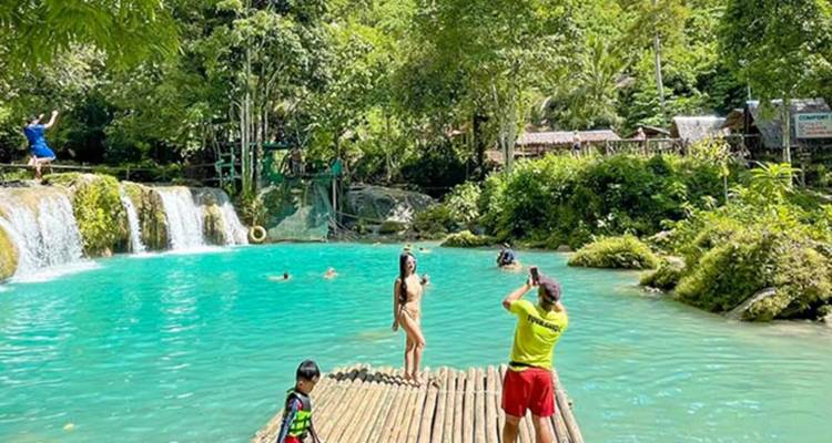 People enjoying a natural spring with waterfalls and lush surroundings.