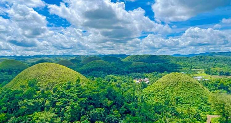 Chocolate Hills landscape under a bright blue sky with clouds.