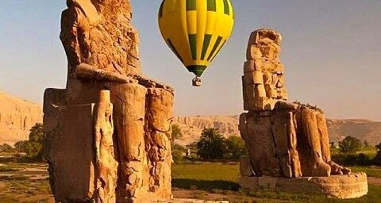 Hot air balloon rising over ancient Egyptian statues.